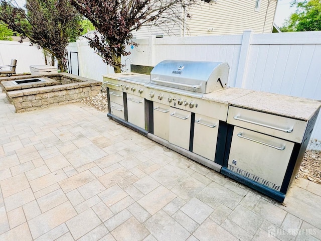 view of patio with exterior kitchen, fence, and a grill