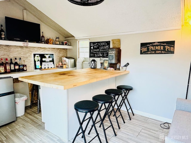 indoor dry bar featuring freestanding refrigerator, wood finished floors, vaulted ceiling, and baseboards