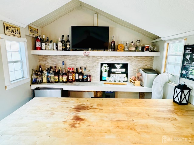 indoor dry bar with vaulted ceiling and tasteful backsplash