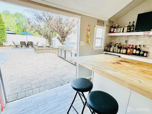 indoor dry bar featuring vaulted ceiling, backsplash, and a textured ceiling