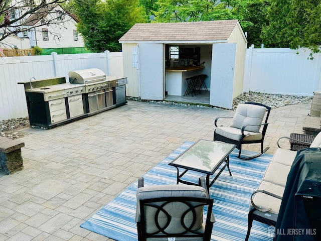 view of patio with exterior kitchen, a fenced backyard, an outdoor structure, a grill, and a sink
