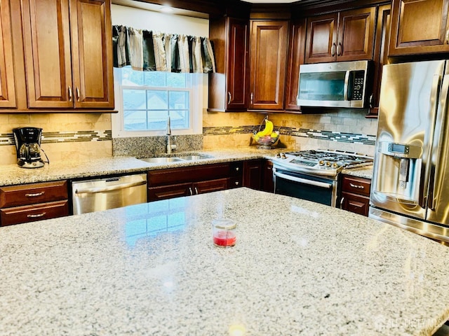 kitchen featuring stainless steel appliances, a sink, light stone counters, and tasteful backsplash