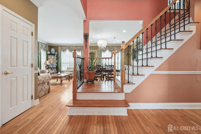 staircase with hardwood / wood-style flooring, crown molding, baseboards, and a chandelier