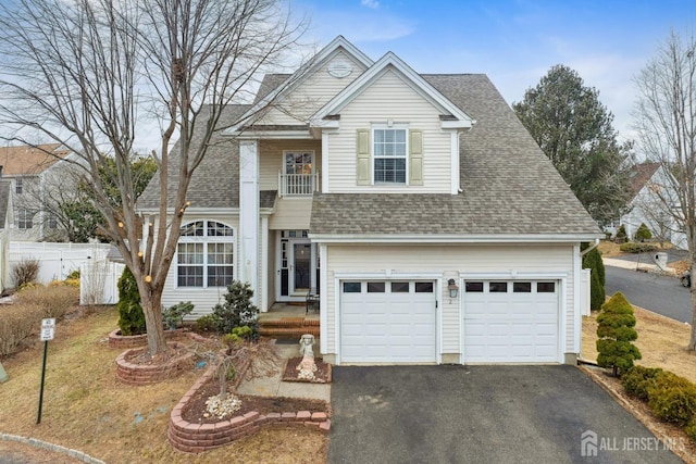 traditional home with aphalt driveway, an attached garage, roof with shingles, and fence