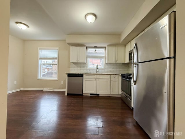kitchen with dark wood-type flooring, white cabinetry, tasteful backsplash, a sink, and stainless steel appliances