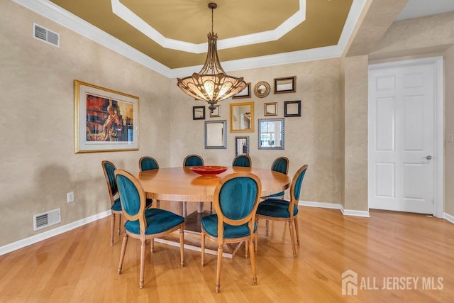 dining room featuring a notable chandelier, hardwood / wood-style flooring, ornamental molding, and a raised ceiling