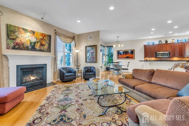 living room featuring a tiled fireplace, a notable chandelier, and light hardwood / wood-style floors