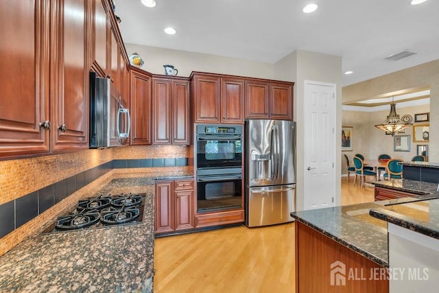 kitchen featuring an inviting chandelier, dark stone counters, hanging light fixtures, black appliances, and light wood-type flooring