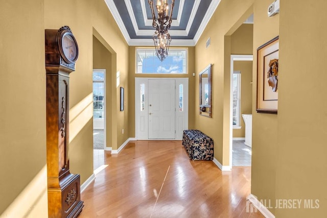 foyer with a notable chandelier, a tray ceiling, ornamental molding, and hardwood / wood-style floors