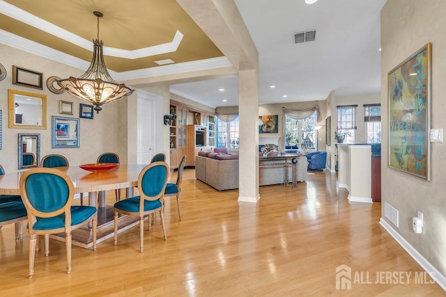 dining room with crown molding, a notable chandelier, light wood-type flooring, and a tray ceiling