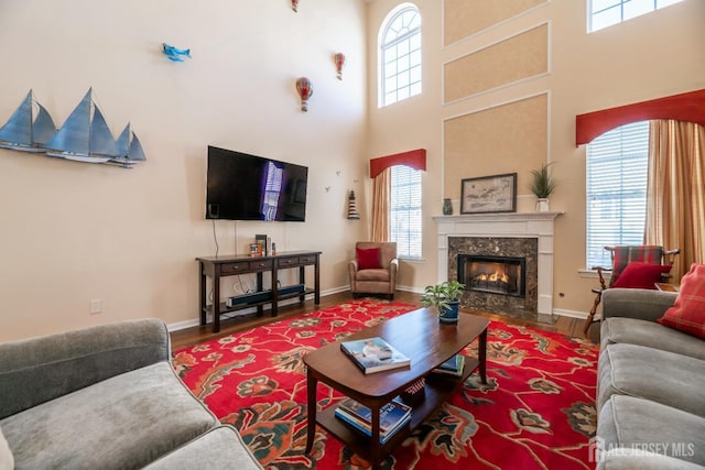 living room with a towering ceiling, a wealth of natural light, a premium fireplace, and wood-type flooring