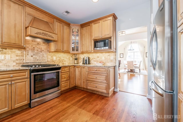 kitchen with premium range hood, stainless steel appliances, tasteful backsplash, light stone countertops, and light wood-type flooring