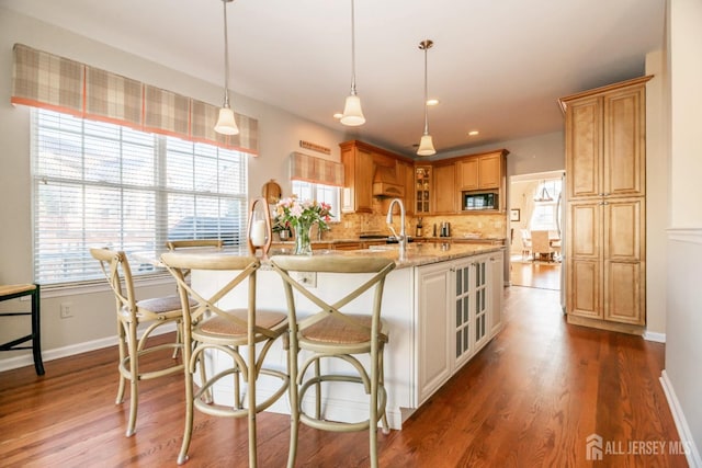 kitchen with built in microwave, tasteful backsplash, decorative light fixtures, dark hardwood / wood-style floors, and light stone countertops