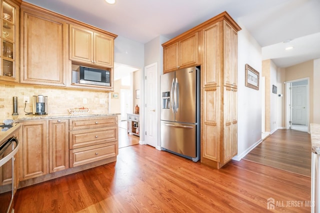 kitchen with light stone counters, decorative backsplash, hardwood / wood-style flooring, and appliances with stainless steel finishes