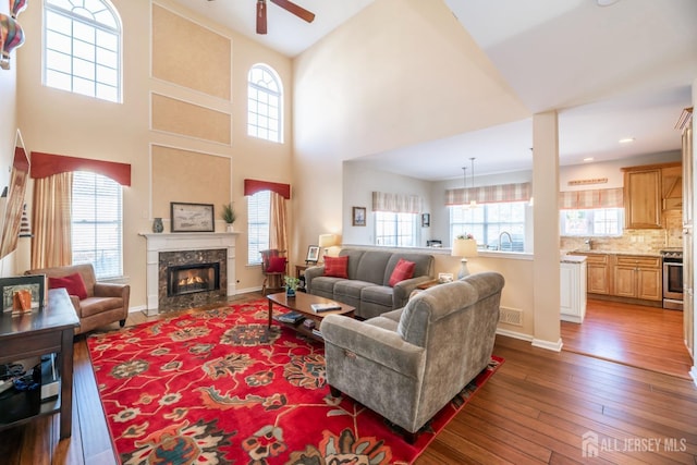 living room featuring sink, dark wood-type flooring, a premium fireplace, ceiling fan, and a high ceiling