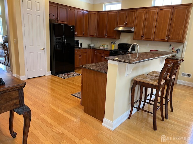 9 Copernicus Ct, East Windsor, NJ 08512 - kitchen with black appliances, under cabinet range hood, light wood finished floors, a kitchen breakfast bar, and dark stone counters