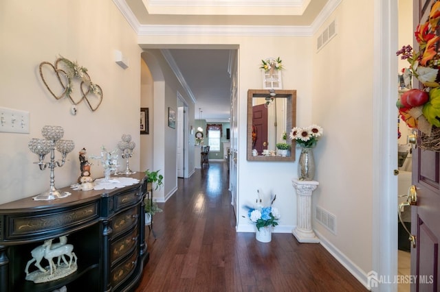 hallway with wood finished floors, ornamental molding, arched walkways, and baseboards