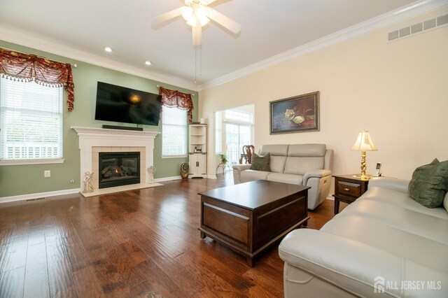 living area featuring a ceiling fan, ornamental molding, a fireplace, baseboards, and dark wood finished floors