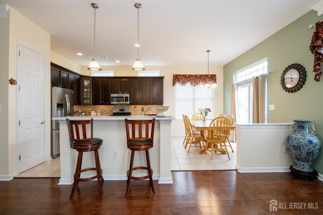kitchen featuring appliances with stainless steel finishes, glass insert cabinets, light countertops, dark brown cabinets, and tasteful backsplash