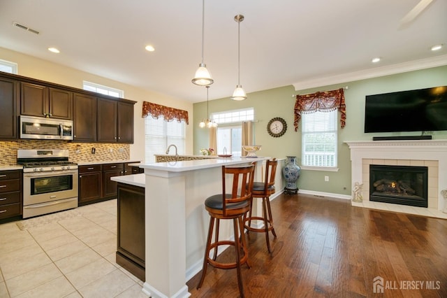kitchen featuring appliances with stainless steel finishes, light countertops, dark brown cabinets, open floor plan, and recessed lighting