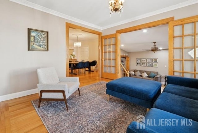 living room featuring wood finished floors, a chandelier, a ceiling fan, baseboards, and crown molding