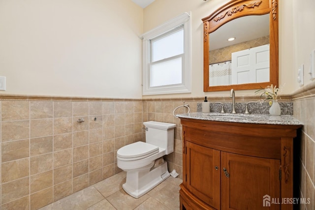full bath with tile walls, tile patterned floors, toilet, wainscoting, and vanity