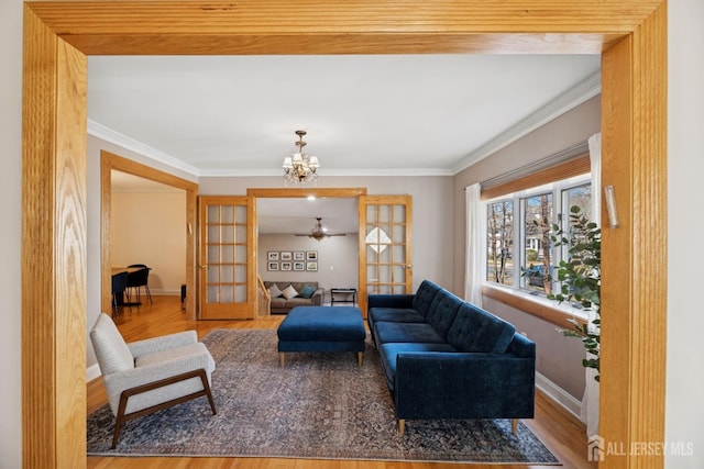 living room featuring wood finished floors, baseboards, a chandelier, ornamental molding, and a ceiling fan