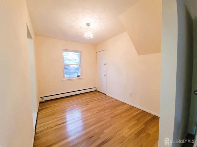 empty room with a baseboard heating unit, baseboards, and light wood finished floors