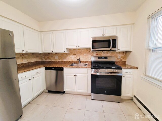 kitchen with decorative backsplash, a baseboard radiator, appliances with stainless steel finishes, white cabinetry, and a sink