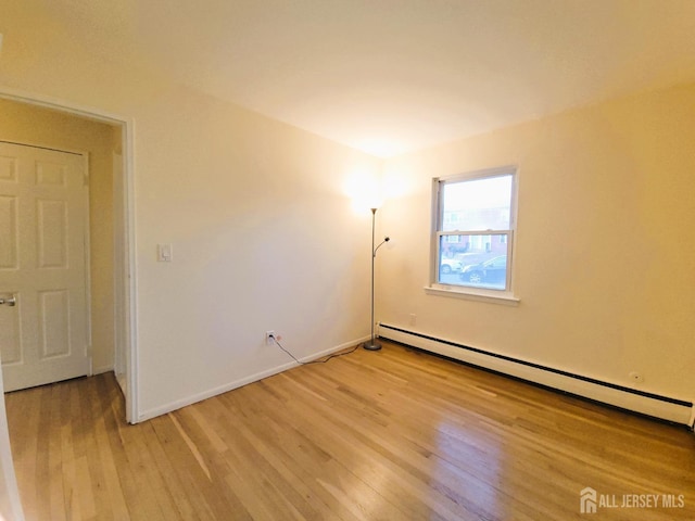 empty room with light wood finished floors, baseboards, and a baseboard heating unit