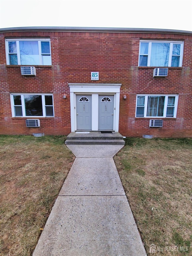 entrance to property featuring a yard, brick siding, and a wall mounted AC