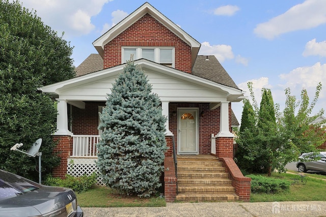 view of front facade with a porch, brick siding, and roof with shingles