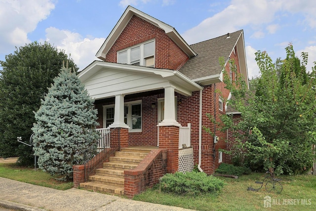 view of front of house featuring brick siding, covered porch, and a shingled roof