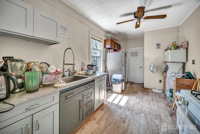 kitchen with light countertops, a ceiling fan, a sink, white appliances, and light wood-type flooring