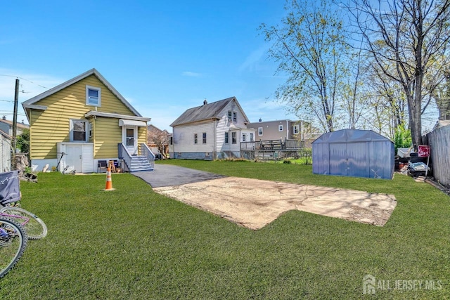 rear view of property featuring a lawn, fence, an outbuilding, and a storage unit