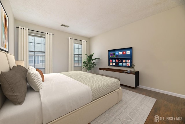 bedroom featuring baseboards, wood finished floors, visible vents, and a textured ceiling