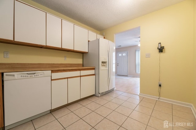 kitchen featuring a textured ceiling, white cabinetry, white appliances, light tile patterned flooring, and baseboards