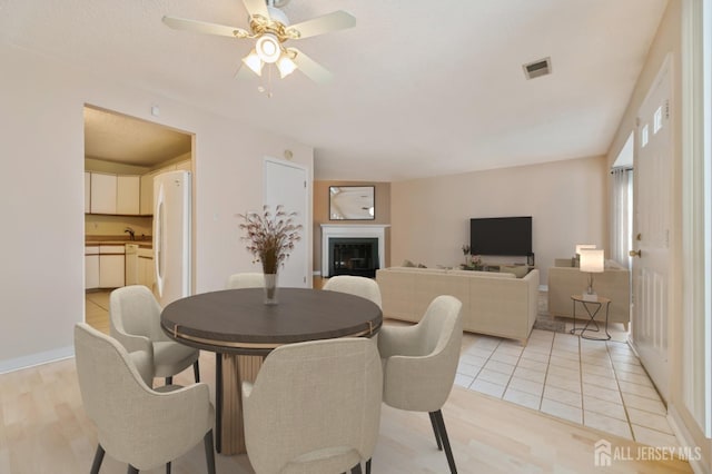 dining room featuring visible vents, a glass covered fireplace, a ceiling fan, and light wood-style flooring