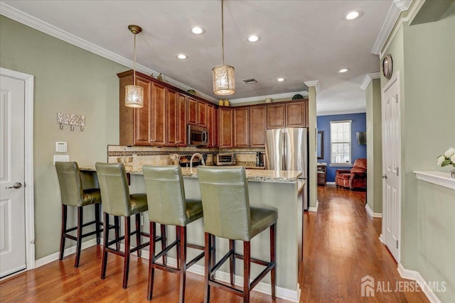 kitchen featuring decorative light fixtures, a breakfast bar, ornamental molding, and stainless steel appliances