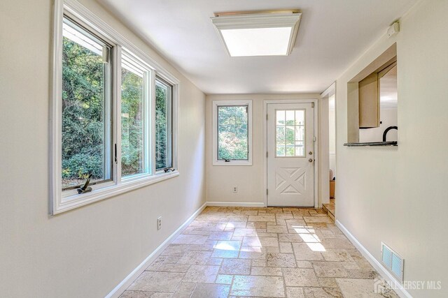 doorway to outside featuring baseboards, visible vents, and stone tile flooring