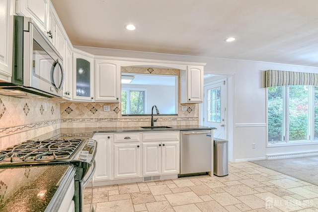 kitchen featuring stainless steel appliances, a sink, white cabinets, dark stone counters, and stone tile flooring