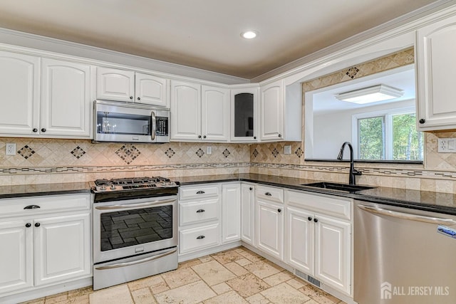 kitchen featuring stainless steel appliances, stone tile flooring, decorative backsplash, white cabinetry, and a sink