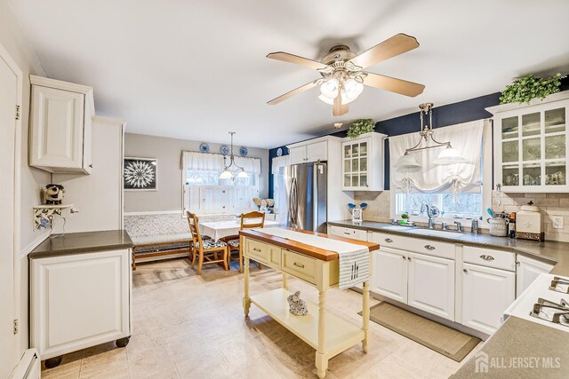 kitchen with sink, white cabinets, stainless steel fridge, baseboard heating, and pendant lighting