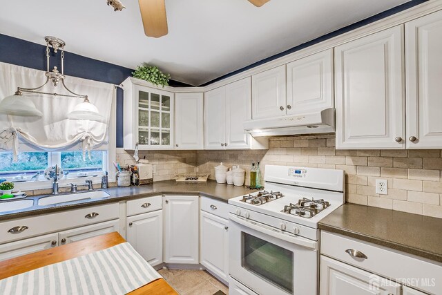 kitchen featuring hanging light fixtures, white gas range oven, sink, white cabinets, and tasteful backsplash