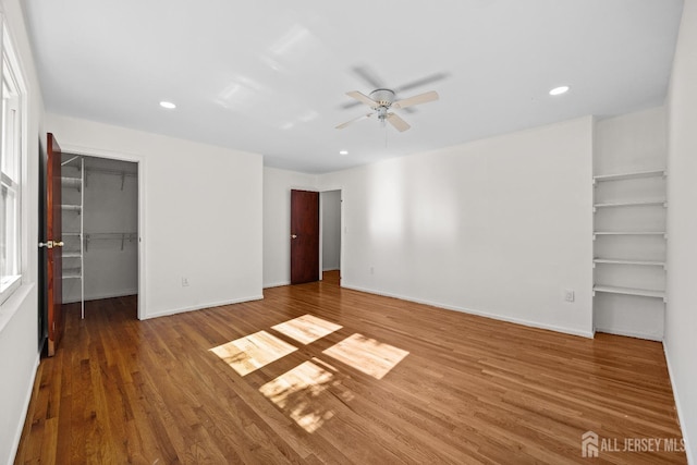 unfurnished bedroom featuring a spacious closet, baseboards, wood finished floors, and recessed lighting