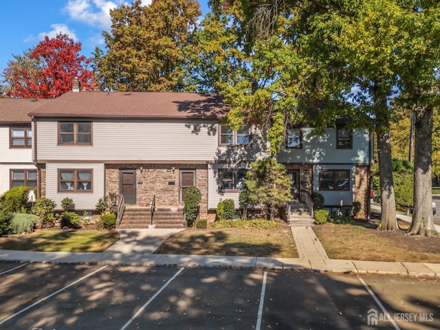 view of property featuring a front yard, uncovered parking, and brick siding