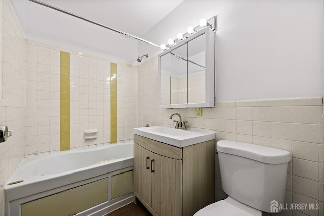 full bathroom with a wainscoted wall, tile walls, toilet, washtub / shower combination, and vanity