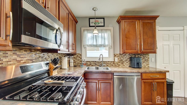 27 Carlton Ave, Monroe, NJ 08831 - kitchen featuring appliances with stainless steel finishes, a sink, tasteful backsplash, hanging light fixtures, and brown cabinets
