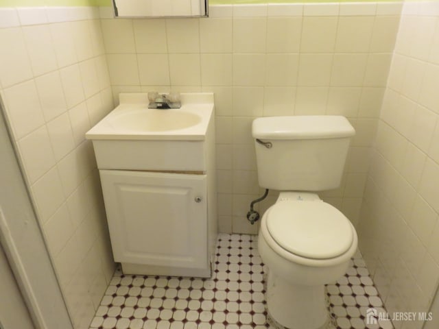 half bathroom with tile walls, vanity, tile patterned floors, and toilet