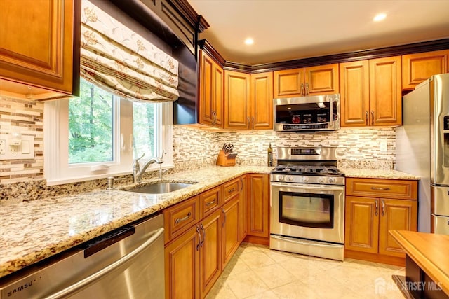 kitchen featuring a sink, light stone counters, appliances with stainless steel finishes, and brown cabinetry